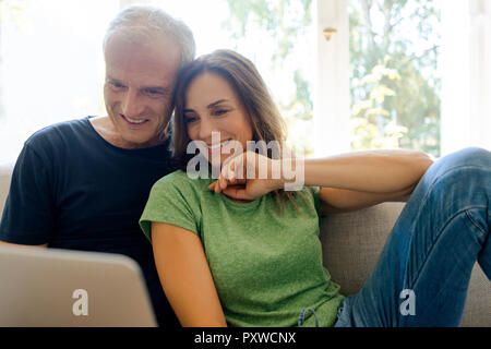 Lächelnd reifes Paar sitzt auf der Couch zu Hause teilen Laptop Stockfoto