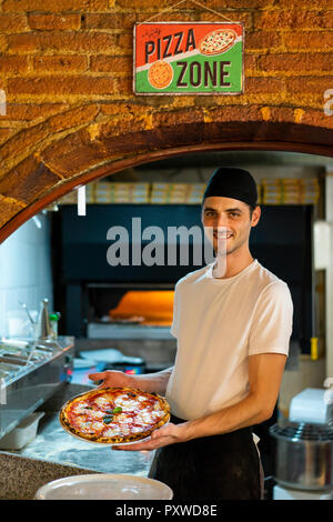 Portrait von lächelnden Pizza Bäcker Holding eine Pizza in der Küche Stockfoto