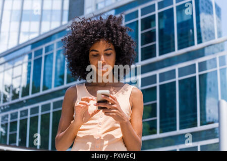 Deutschland, Frankfurt, Porträt der jungen Frau mit dem lockigen Haar mit Smartphone Stockfoto