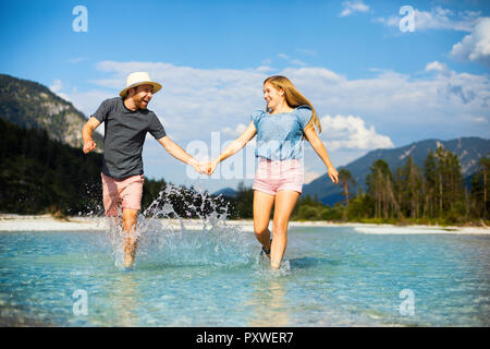 Junges Paar halten sich an den Händen und laufen durch Wasser Stockfoto