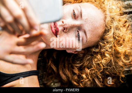 Porträt der rothaarige junge Frau liegt auf der Werkbank mit Handy Stockfoto