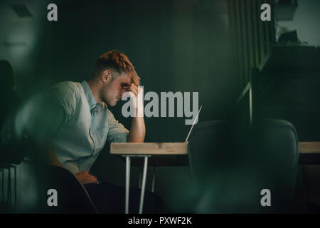 Müde Mann sitzt im Büro, zu spät in seinem Start-up-Unternehmen Stockfoto