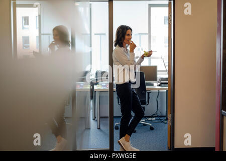 Geschäftsfrau, die sich in Büro, essen Trauben Stockfoto