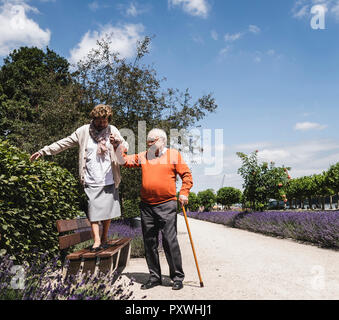 Senior Paar, das Spaß im Park, älterer Mann helfen Womn auf der Werkbank zu Balance Stockfoto