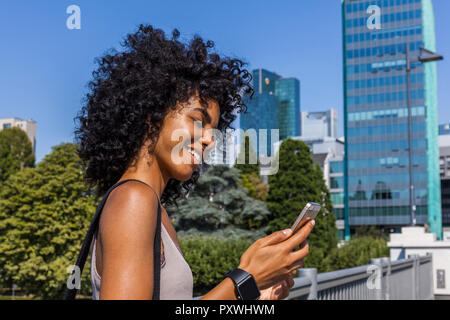 Deutschland, Frankfurt, lächelnden jungen Frau mit lockigem Haar an Zelle Telefon Stockfoto