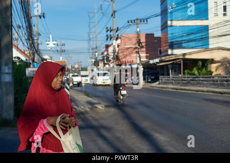 Eine muslimische Frau in der Nähe der Hauptmoschee in muslimisch dominierten Bang Tao, Phuket, Thailand, Peering über die Hauptstraße, Netzkabel Overhead Stockfoto