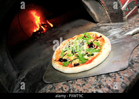 Schwarze Oliven, italienische Wurst, Schinken, frischen Rucola und Parmesan Pizza, in einem traditionellen Holzofen serviert Pizza Stockfoto