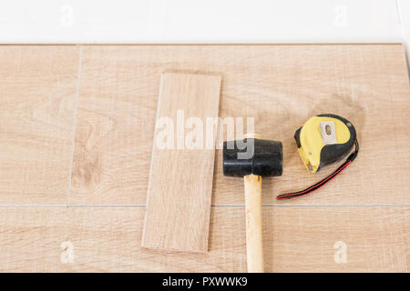 Installation von Laminat Parkett in Innenraum. Auf dem Boden verschiedene Tischler Werkzeuge liegen. Hammer und Maßband. Konzept der Reparatur im Haus. Stockfoto