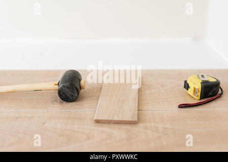 Installation von Laminat Parkett in Innenraum. Auf dem Boden verschiedene Tischler Werkzeuge liegen. Hammer und Maßband. Konzept der Reparatur im Haus. Stockfoto