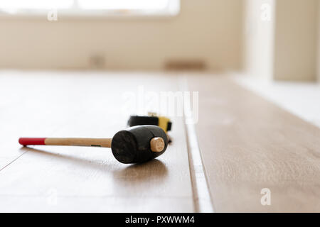 Installation von Laminat Parkett in Innenraum. Auf dem Boden verschiedene Tischler Werkzeuge liegen. Hammer und Maßband. Konzept der Reparatur im Haus. Stockfoto