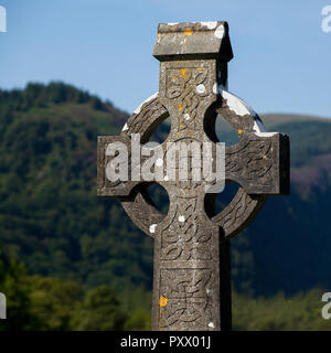 Eine geschnitzt, Stein keltisches Kreuz in Irland, mit grünen Hügeln und einem blauen Himmel hinter sich. Moos wächst auf dem Mauerwerk der Alten ist. Stockfoto