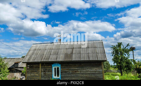 Ein wunderschöner Storch Vogel mit rotem Schnabel sitzt auf einem Schornstein eines Holz- Haus in einem Dorf gegen einen schönen blauen Himmel mit weißen Wolken. Agritourismus in Stockfoto