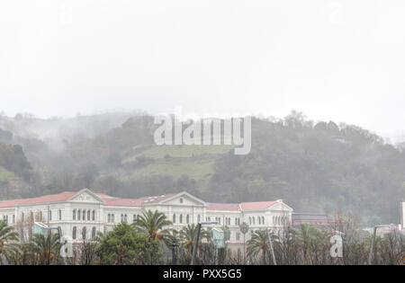 Die neoklassische Universität Deusto in Bilbao, Baskenland, Spanien, vor einem grünen und foggy Hill während einer Winter regnerisch und bewölkt Tag. Stockfoto