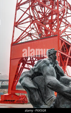 Hombre Tuercebarras (bar biegen Mann) Skulptur vor der Roten Grua Carola (Carola Kran) in Bilbao, Baskenland, Spanien, während eines regnerischen Tag Stockfoto