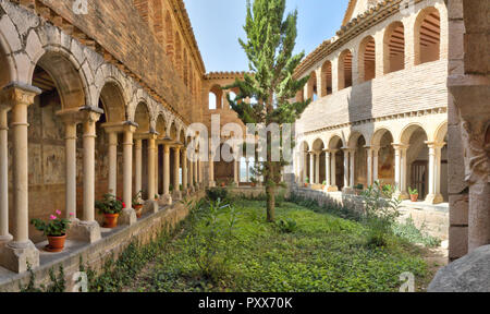 Der Kreuzgang mit romanischen Bögen, einen Tannenbaum und mittelalterlichen Fresken an einem sonnigen Tag in der Colegiata de Santa Maria la Mayor von Alquezar, Spanien Stockfoto