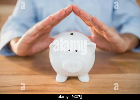 Den mittleren Abschnitt der Mann, der ein Dach Geste auf piggy Bank Stockfoto