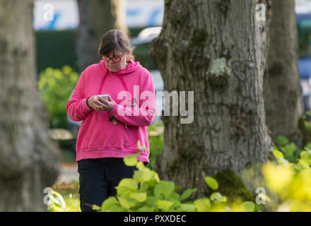 Frau mittleren Alters, die Eingabe auf dem Smartphone beim Gehen, in Großbritannien. Stockfoto