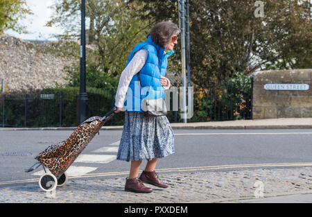 Ältere Frau zu Fuß, während Sie einen Einkaufswagen in Großbritannien, Seitenansicht. Stockfoto