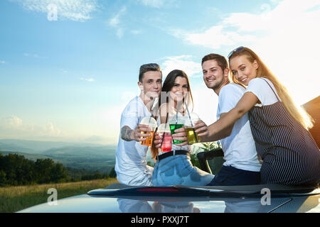 Enge Freunde Sommer zusammen verbringen. Zwei Paare holding Limonade und klirren Gläser während der Sitzung in Cabrio. Charmante Mädchen und schönen Männern an Kamera suchen und lächelnd. Stockfoto