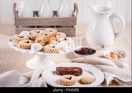 Italienische Kekse mit Marmelade, Mandeln, Milch Flaschen und Krug auf eine Tischdecke. Stockfoto