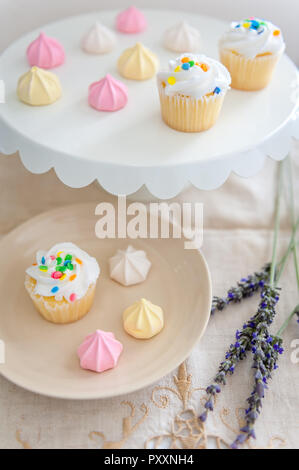 Einen Kuchen Platte und Dessertteller gefüllt mit Konfetti bestreut Cupcakes und pastellfarbenen Meringue biss Cookies. Stockfoto