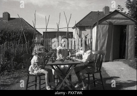 1950, historische, drei junge Kinder zusammen draußen im Garten sitzen spielen Domino an einem Tisch, England, UK. Stockfoto