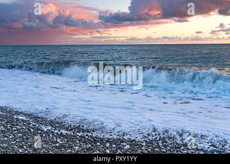 Marine mit rosa Wolken und Wellen auf einem Kieselstrand. Stockfoto