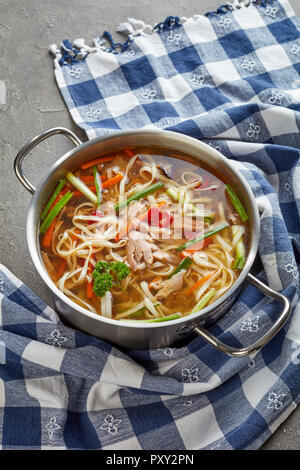 Übrig gebliebene Pekingente udon Nudeln Gemüse Suppe in eine Kasserolle auf einer konkreten Tabelle mit Küchentuch, Ansicht von oben Stockfoto