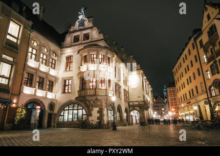 Munich, Bayern, Deutschland - Dezember 6, 2017: Beleuchtete Hofbräuhaus mit Fahrrädern und verschwommene Menschen am Platzl Platz in der Nacht in München Stockfoto