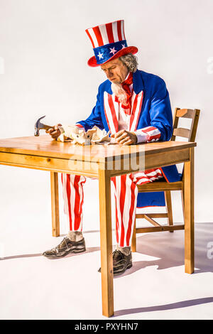 Eine traurige Uncle Sam sitzen über eine zerbrochene piggy Bank Holding einen Hammer. Konzeptionelle Schuß für Treasury, Defizite, Bank, Sparen, Steuern. Stockfoto