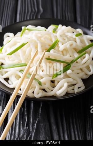 Klassische udon Nudeln mit grünen Zwiebeln close-up auf einem Schild auf einem Schwarzen Tisch. Vertikale Stockfoto