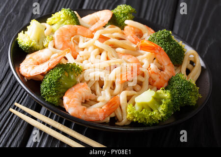 Im asiatischen Stil udon Nudeln mit Garnelen, Brokkoli und Sojasauce close-up auf einem Teller auf den Tisch. Horizontale Stockfoto