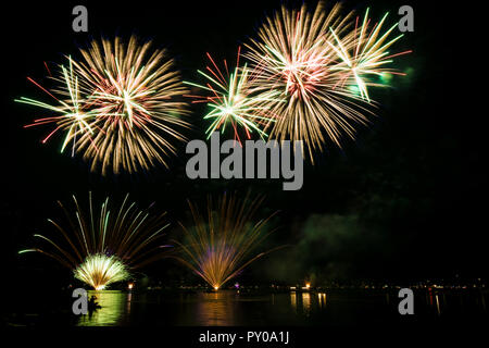 Buntes Feuerwerk Explosionen in der Nacht im Wasser widerspiegelt Stockfoto