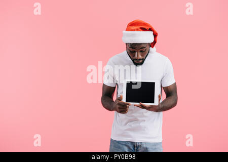 Portrait der afrikanischen amerikanischen Mann in santa claus Hut mit Tablette mit leeren Bildschirm isoliert auf Rosa Stockfoto