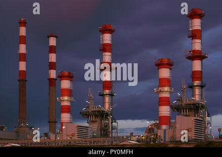 Ein Teil der vielen Schornsteine einer großen Ölraffinerie und Triebwerk in einem bewölkten Nacht Stockfoto