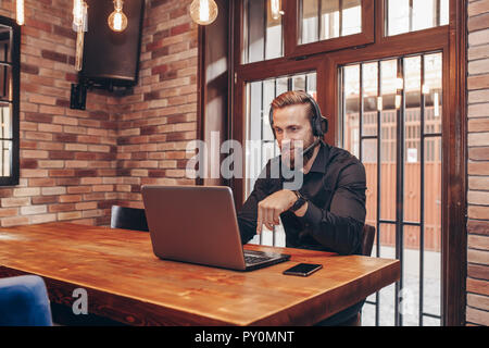 Junge Bartgeier Spezialist mit Ohrhörer im Gespräch mit Arbeitgeber durch Videokonferenz während online Interview Stockfoto