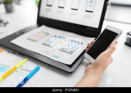 Web Designer mit Smartphone und Laptop im Büro Stockfoto
