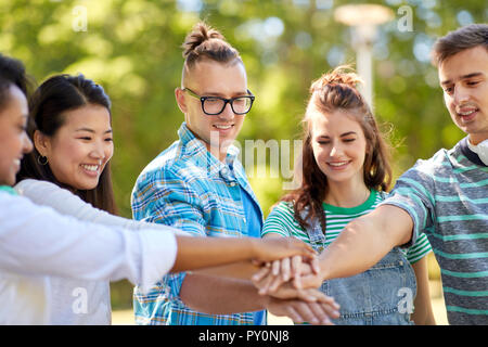 Glücklich lächelnde Freunde stapeln Hände in Park Stockfoto