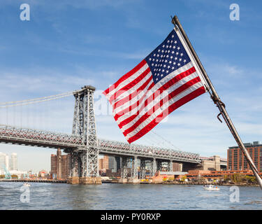 Eine amerikanische Flagge, die mit einem Boot auf dem East River in New York City. Im Hintergrund ist die Williamsburg Bridge Manhattan anschließen Stockfoto