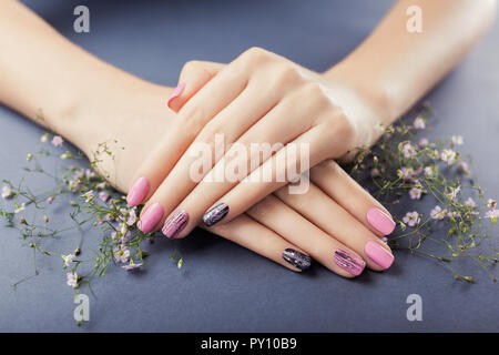 Rosa und Schwarz Maniküre mit Blumen auf grauem Hintergrund. Nail Art Körperpflege Stockfoto