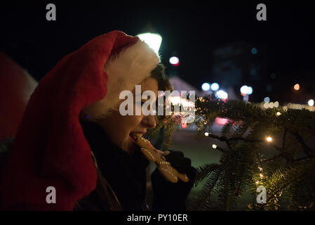 Lächelnde Frau trägt ein Santa hat Essen eine Gingerbread Man Stockfoto