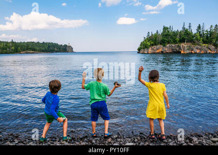 Drei Kinder werfen Steine in einen See, Split Rock Lighthouse State Park, Minnesota, USA Stockfoto