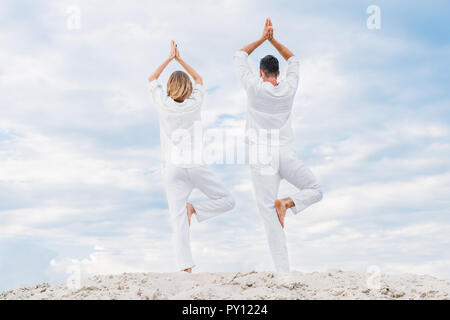 Ansicht der Rückseite des Paares in weißen Kleidern mit Yoga in die baumhaltung (Vrksasana) auf Sand dune Stockfoto