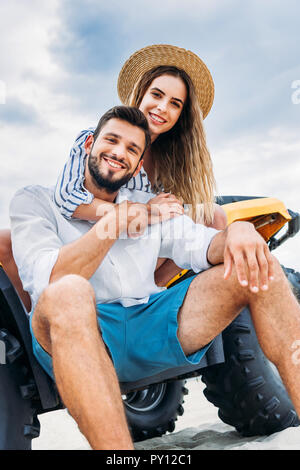 Ansicht von unten auf das glückliche junge Paare sitzen auf ATV vor Wolkenhimmel Stockfoto