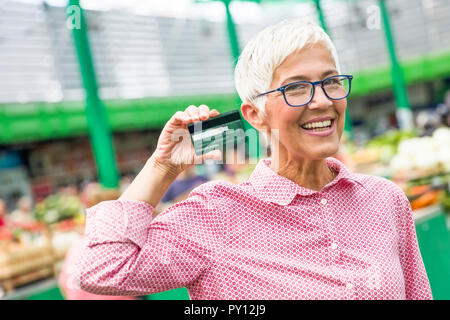 Portrait der älteren Frau hält Kreditkarte auf den Markt Stockfoto