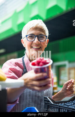 Portrait der älteren Frau verkauft Himbeeren auf dem Markt Stockfoto