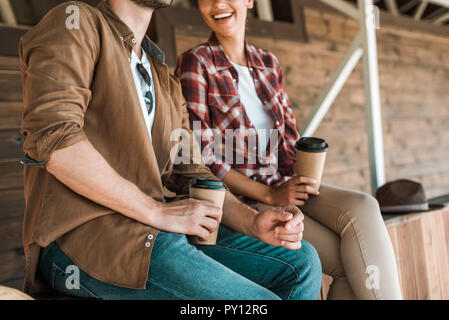 Zugeschnittenes Bild von Cowboy und Cowgirl sitzen mit Einweg kaffeetassen an der Ranch Stockfoto
