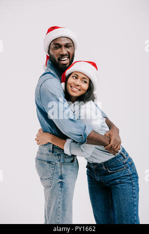 Lächelnd afrikanische amerikanische Ehepaar in Santa Hüte isoliert umarmen auf Weiß Stockfoto