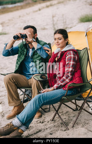 Paar mit Fernglas ruht auf Stühlen auf Camping Stockfoto