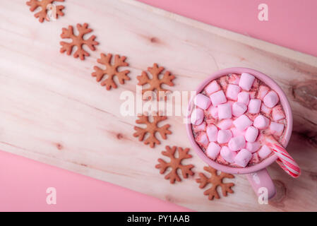 Winter Süßigkeiten in rosa Farbtönen, eine Tasse heiße Schokolade mit Marshmallows und ein Weihnachten Zuckerstange und Schneeflocken geformte Lebkuchen Cookies. Stockfoto